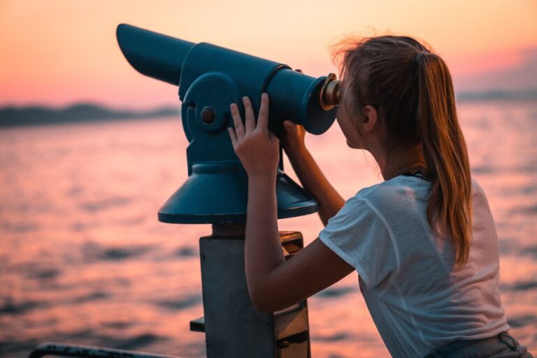 view-female-using-telescope-looking-into-sunset-beach-from-pier_181624-23921